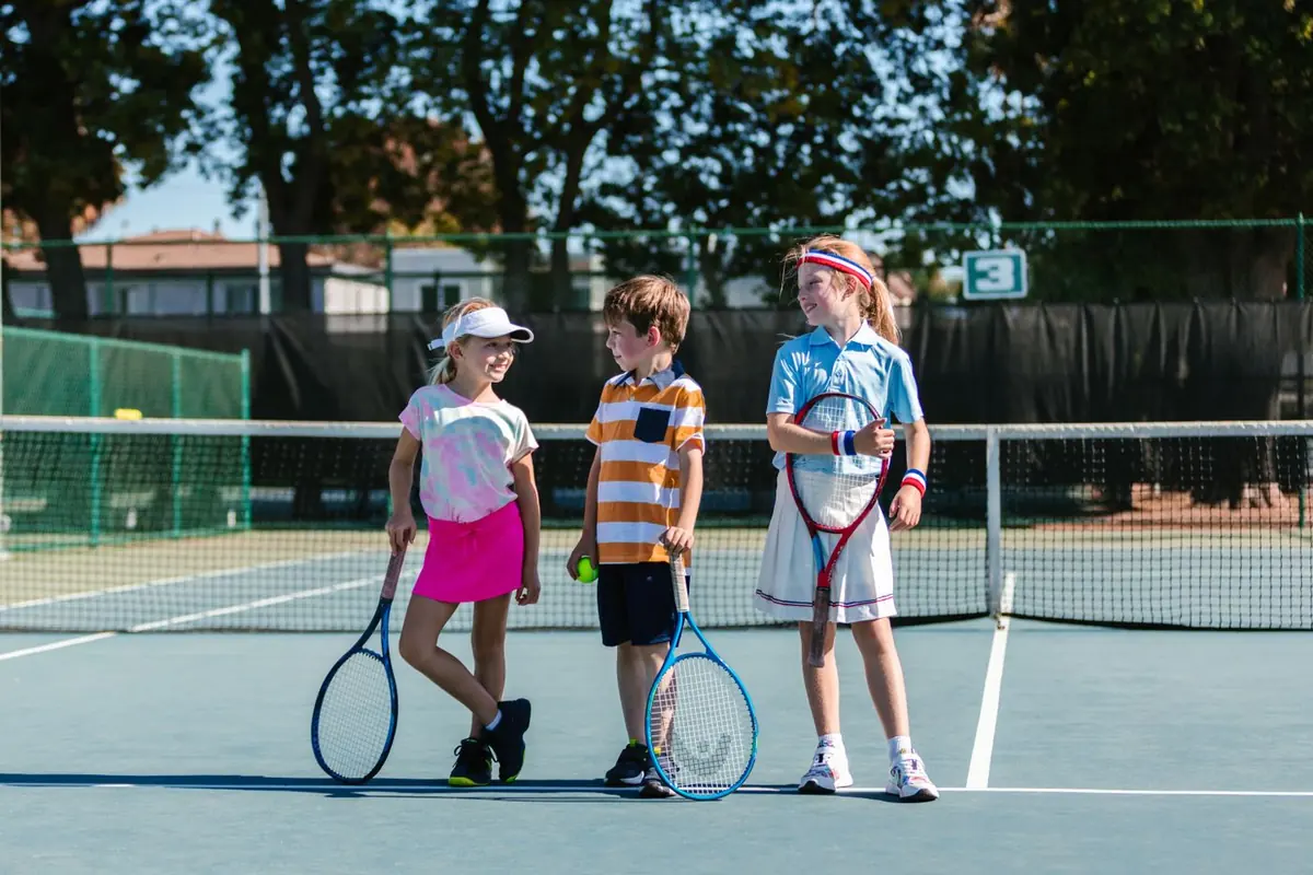 Tres niños con raquetas de tenis en la pista